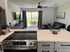 A modern kitchen with a built-in oven, a dining area with a table and chairs, a sofa, and a sliding glass door leading to an outdoor patio. - Jamaica Royale 017 Close to the Pool! (Siesta Key)
