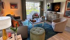Un salon moderne comprenant un canapé, un pouf, une table basse et un téléviseur.