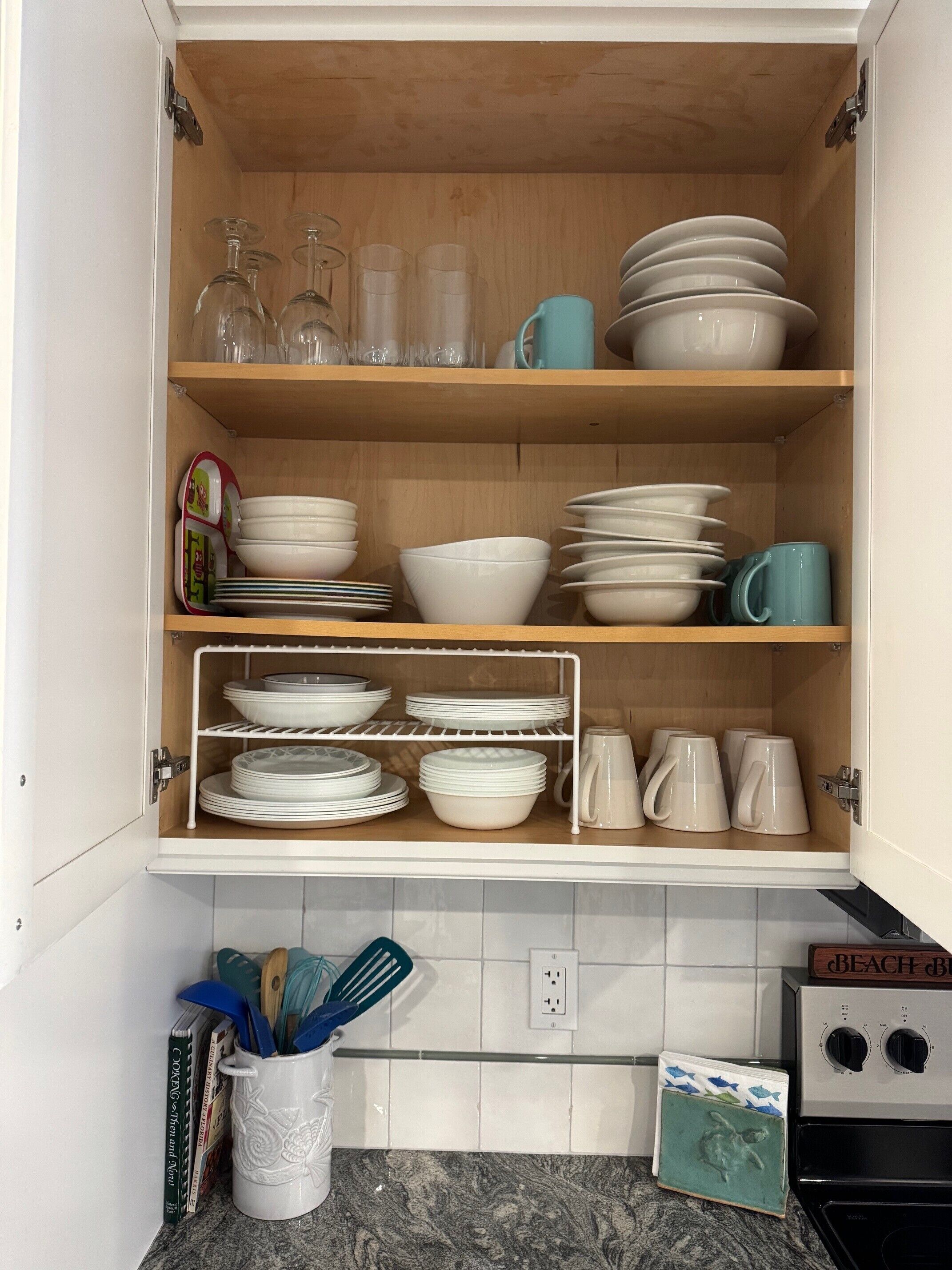 A kitchen with wooden shelves holding various dishes, glasses, and a coffee maker.