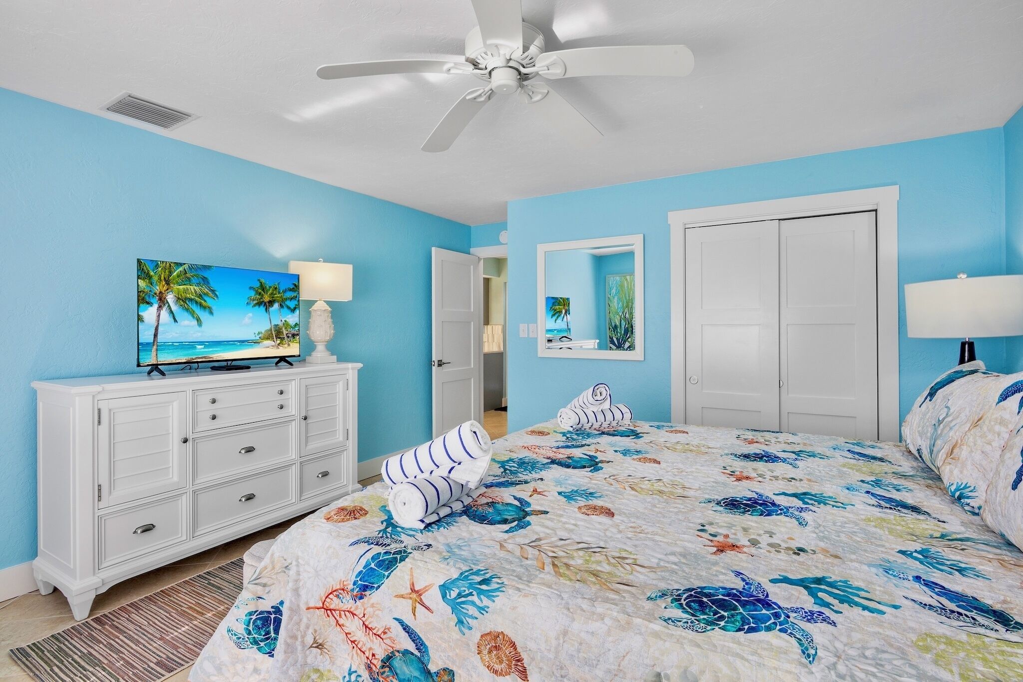 A bedroom with a bed, a TV, a dresser, and a ceiling fan.