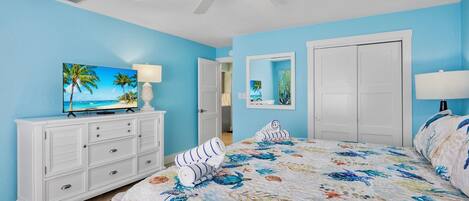 A bedroom with a bed, a TV, a dresser, and a ceiling fan.