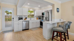 A modern kitchen with white cabinetry, stainless steel appliances, and a bar area with two bar stools. - Jamaica Royale 028 Washer and Dryer Plus Half Bath (Siesta Key)