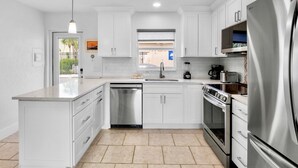 A modern kitchen with white cabinetry, stainless steel appliances, a dishwasher, and a large refrigerator. - Jamaica Royale 030 Nicely Updated! (Siesta Key)