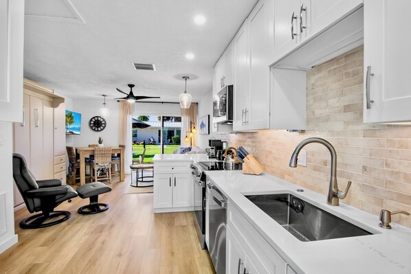 A modern kitchen with white cabinets, a stainless steel sink, and a dining area with a view of the outdoors.