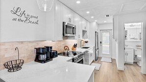 A modern kitchen with white cabinetry, a large island, a microwave, and a coffee maker. - Jamaica Royale 031 Nicely Updated! (Siesta Key)