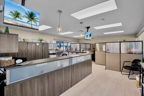 A modern hotel lobby with a reception desk, seating area, and a large TV screen displaying a beach scene.