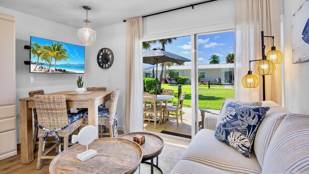 A modern living room with a sofa, dining table, chairs, and a TV displaying a beach scene. - Jamaica Royale 031 Nicely Updated! (Siesta Key)
