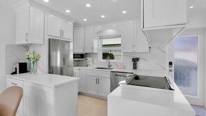 A modern kitchen with white cabinetry, a stainless steel refrigerator, a microwave, and a built-in oven. - Jamaica Royale 033 Close to pool! (Siesta Key)