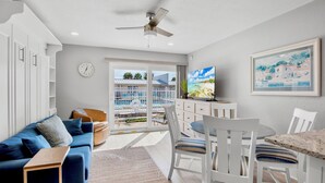 Ein modernes Wohnzimmer mit einem blauen Sofa, einem weißen Esstisch und einem Deckenventilator.