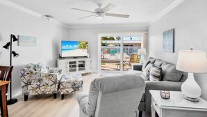 Un salon équipé d’un téléviseur, d’un canapé, d’un fauteuil et offrant une vue sur une piscine et une plage.