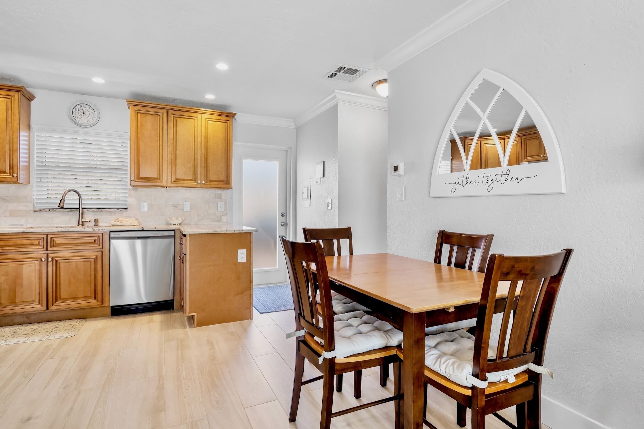 A modern kitchen with wooden cabinets, a dishwasher, and a dining area with a wooden table and chairs.