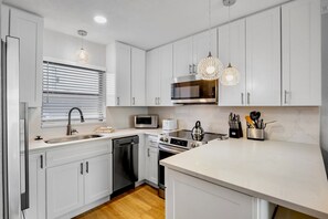Una cocina moderna con armarios blancos, microondas integrado, lavavajillas y estufa.