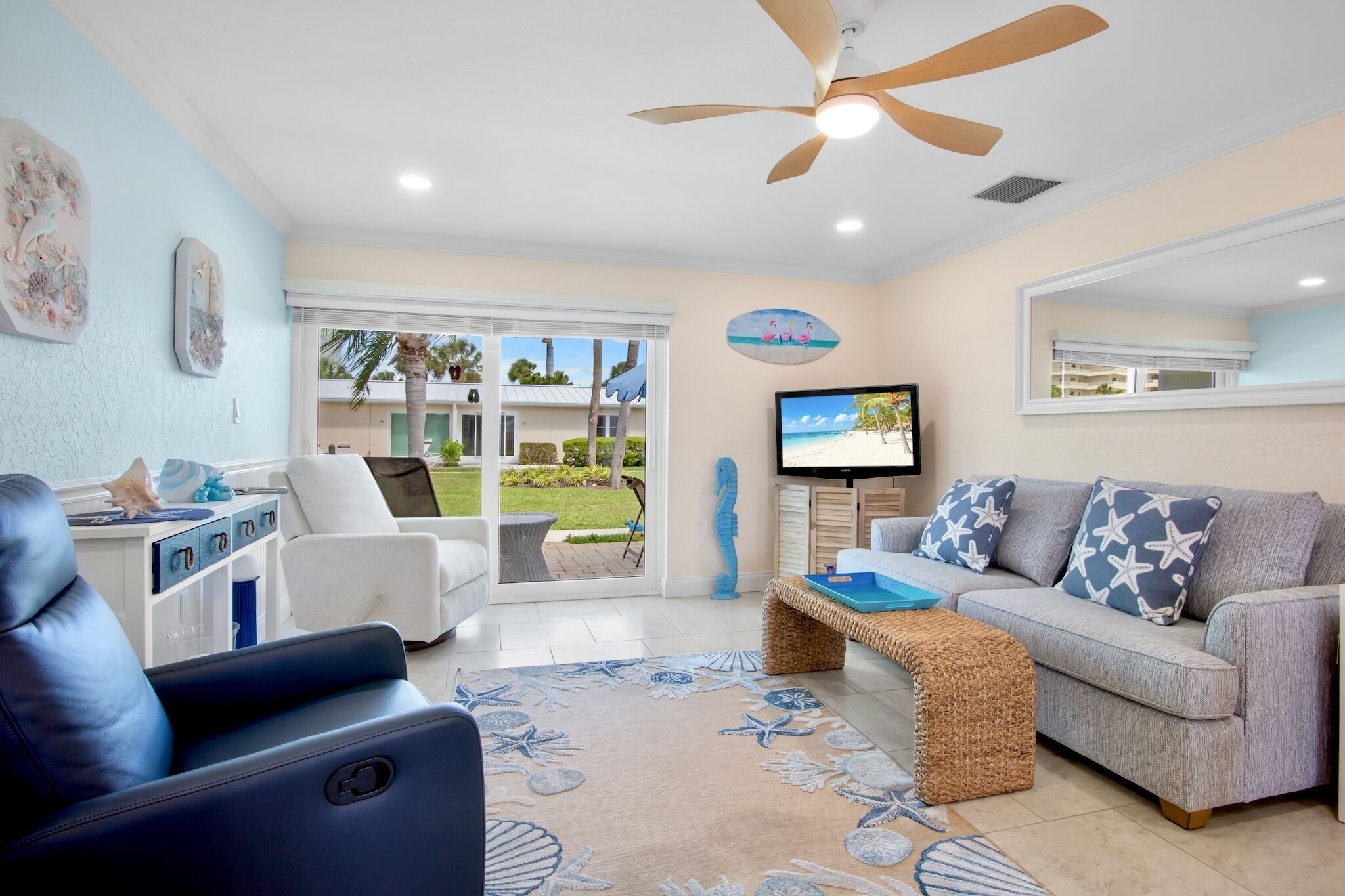 A living room with a ceiling fan, a sofa, a TV, and a view of the outdoors.