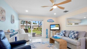 A living room with a ceiling fan, a sofa, a TV, and a view of the outdoors. - Jamaica Royale 058 Beautiful unit and close to the pool! (Siesta Key)