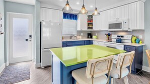 Une cuisine moderne avec des meubles blancs, un îlot central vert et des luminaires suspendus.