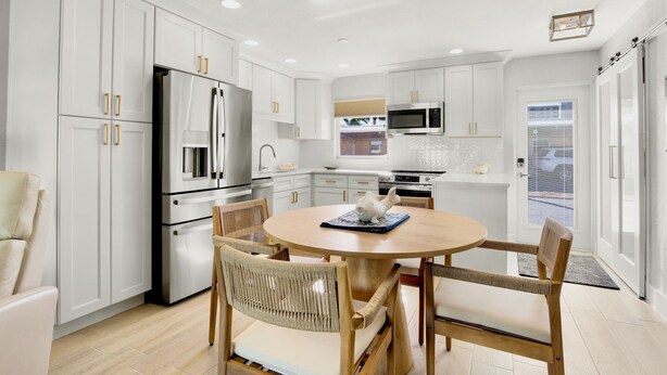 Una cocina moderna con muebles blancos, electrodomésticos de acero inoxidable y una mesa de madera redonda con sillas de mimbre.