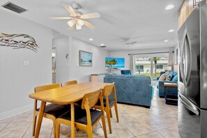 A modern kitchen with a large refrigerator, a dining area with a wooden table and chairs, a blue sofa, and a ceiling fan. - Jamaica Royale 069 Close to the pool! (Siesta Key)