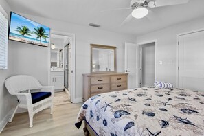 A bedroom with a bed, a dresser, a chair, a ceiling fan, and a TV displaying a beach scene. - Jamaica Royale 069 Close to the pool! (Siesta Key)