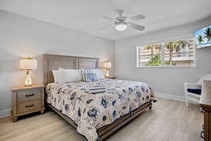 A bedroom with a bed, nightstands, a ceiling fan, a window with blinds, and a chair. - Jamaica Royale 069 Close to the pool! (Siesta Key)