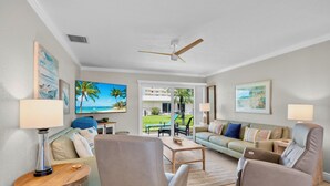 A spacious living room with a large TV, comfortable seating, and a view of the outdoors. - Jamaica Royale 072 Beautiful unit! (Siesta Key)