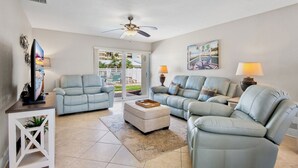 A spacious living room with two light blue leather sofas, a white ottoman, and a ceiling fan. - Jamaica Royale 076 Beautiful and close to the pool! (Siesta Key)