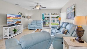 A living room with a TV, a ceiling fan, a sofa, and a view of the outside balcony. - Jamaica Royale 076 Beautiful and close to the pool! (Siesta Key)