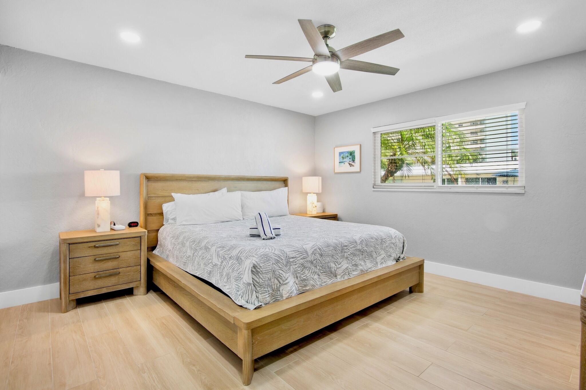 A bedroom with a wooden bed, two bedside tables with lamps, a ceiling fan, and a window with blinds.