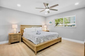 A bedroom with a wooden bed, two bedside tables with lamps, a ceiling fan, and a window with blinds. - Jamaica Royale 078 Updated and close to the beach! (Siesta Key)
