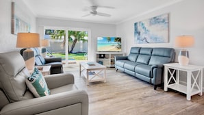 A modern living room with a grey sofa, a white coffee table, and a blue sofa. There is a TV on a stand and a painting on the wall.