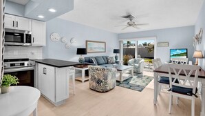 A modern kitchen with white cabinets, a microwave, and an oven. There is a dining area with a table and chairs, and a living room with a sofa and a TV. - Jamaica Royale 083 Updated and close to the beach! (Siesta Key)
