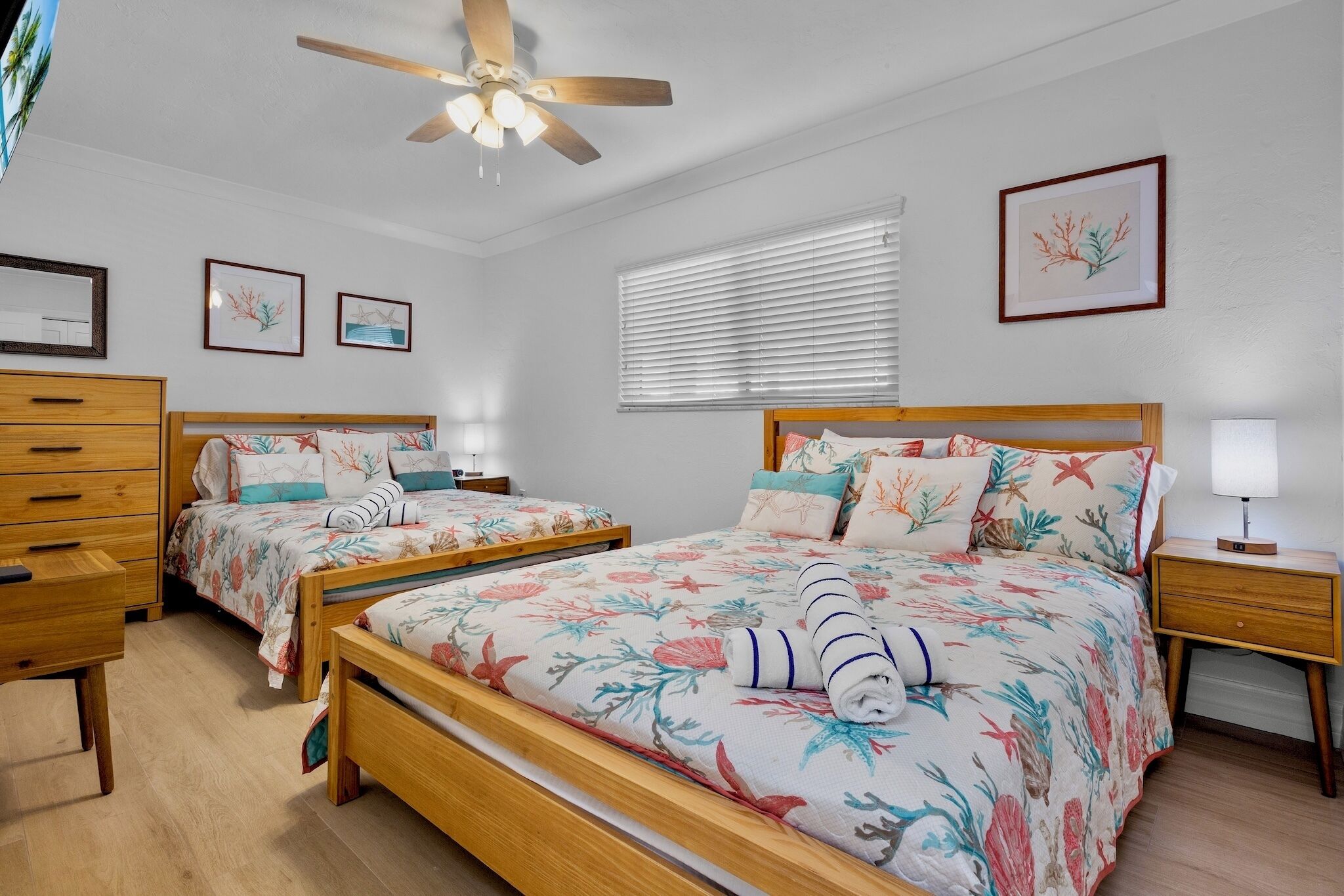 A bedroom with two wooden beds, a ceiling fan, a nightstand with a lamp, and framed artwork on the walls.