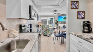 A modern kitchen with a marble countertop, stainless steel sink, and a dining area with a table and chairs. - Jamaica Royale 089 Brand new remodel! (Siesta Key)