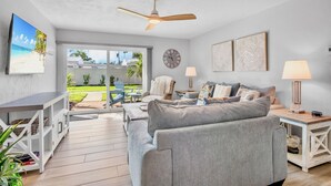 A living room with a grey sofa, a ceiling fan, a clock, and a view of the outdoors. - Jamaica Royale 090 Nicely updated! (Siesta Key)