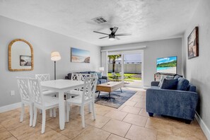 A modern living room with a white dining set, a blue sofa, and a ceiling fan. - Jamaica Royale 093 Updated unit! (Siesta Key)