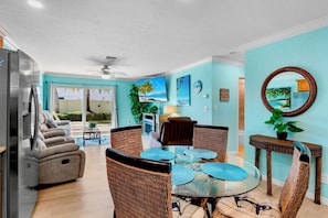 A dining area with wicker chairs, a glass table, and a ceiling fan.