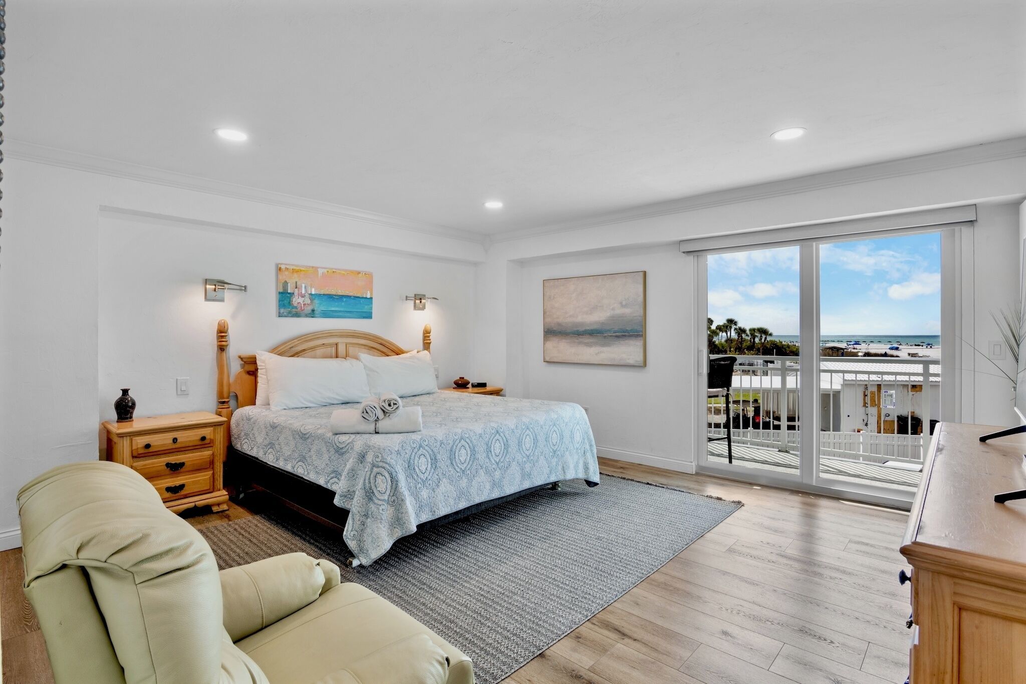 A bedroom with a bed, bedside tables, a chair, a desk, and a balcony with a view.