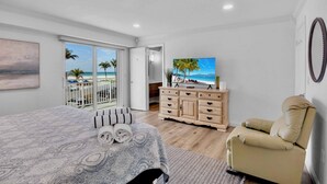 Ein Schlafzimmer mit Bett, Fernseher, Sofa, Kommode und einem Balkon mit Meerblick.
