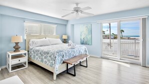 A bedroom with a bed, bedside tables, a bench, a ceiling fan, and a view of the beach through large windows. - Jamaica Royale 205: Spacious Beach Condo with Coastal Charm and Shared Amenities (Siesta Key)