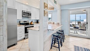 A modern kitchen with white cabinets, a stainless steel refrigerator, a microwave, and a large island with bar stools. - Jamaica Royale 205: Spacious Beach Condo with Coastal Charm and Shared Amenities (Siesta Key)
