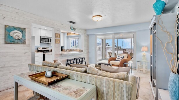 A modern living room with a sofa, a coffee table, and a dining area with a kitchen in the background. - Jamaica Royale 205: Spacious Beach Condo with Coastal Charm and Shared Amenities (Siesta Key)