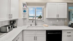Una cucina moderna con mobili bianchi, un tostapane integrato, una macchina da caffè e una finestra vista spiaggia.