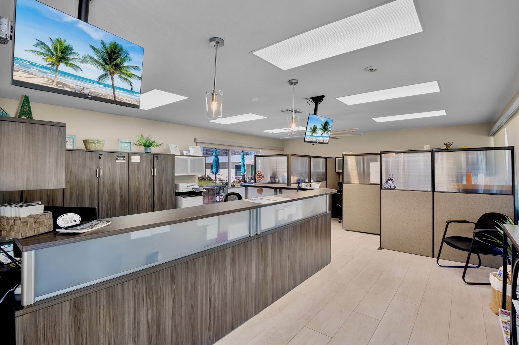 A modern hotel lobby with a reception desk, seating area, and a large TV screen displaying a beach scene.
