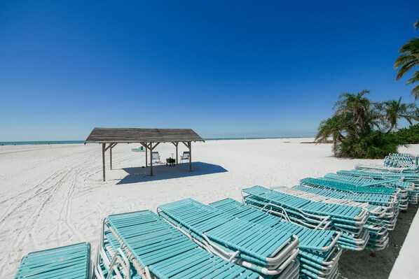 Relax in a tranquil beachside setting with lounge chairs and a shaded pavilion.