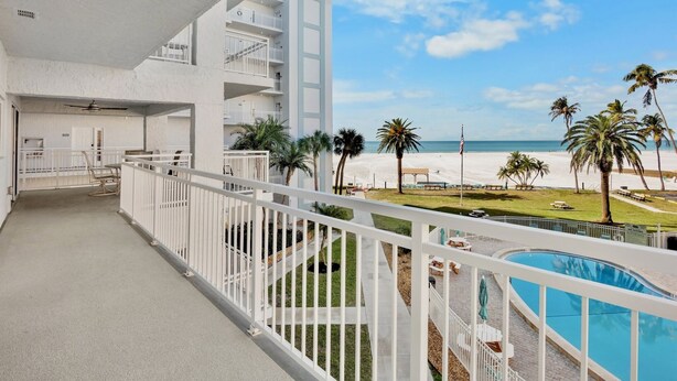 A balcony with a pool, overlooking a beach with palm trees and a clear sky. - Beachfront Condo with Coastal Decor and Community Amenities - Jamaica Royale 306 (Siesta Key)