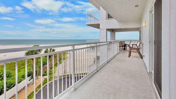 Un balcon avec vue sur la plage, un coin repas avec des chaises et une rambarde blanche.