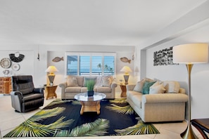A living room with a black and green tropical rug, two sofas, a coffee table, and a floor lamp.