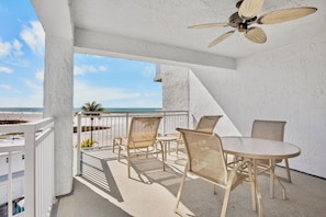 A balcony with a table and chairs, a ceiling fan, and a view of the beach.
