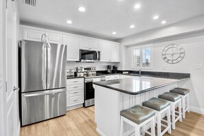 A modern kitchen with stainless steel appliances, a central island with stools, white cabinetry, and a wall clock.