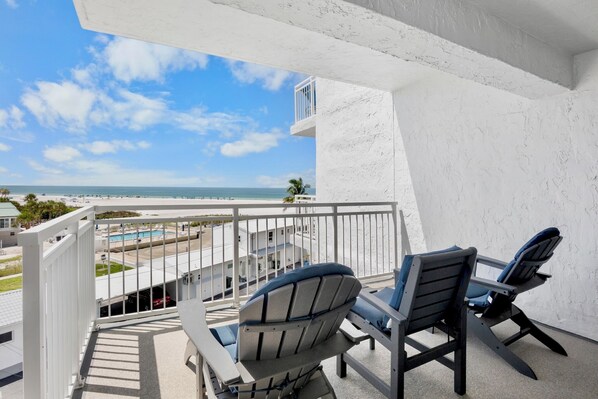 A balcony with two chairs and a view of the beach and ocean.