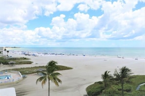 Vista da praia com área de piscina, palmeiras e céu claro.